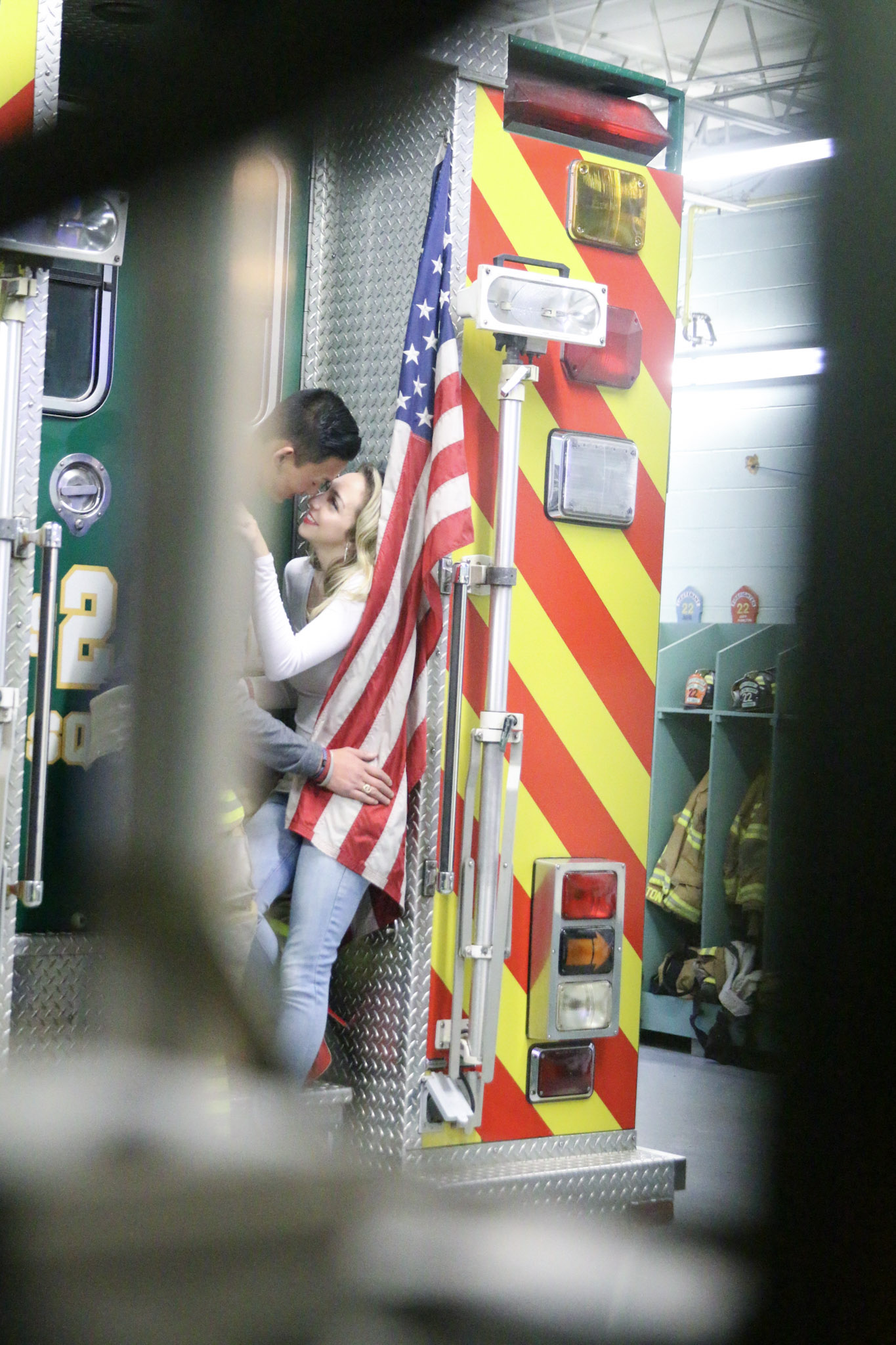 the couple behind the fire truck longingly looking at each other with the American Flag beside them..