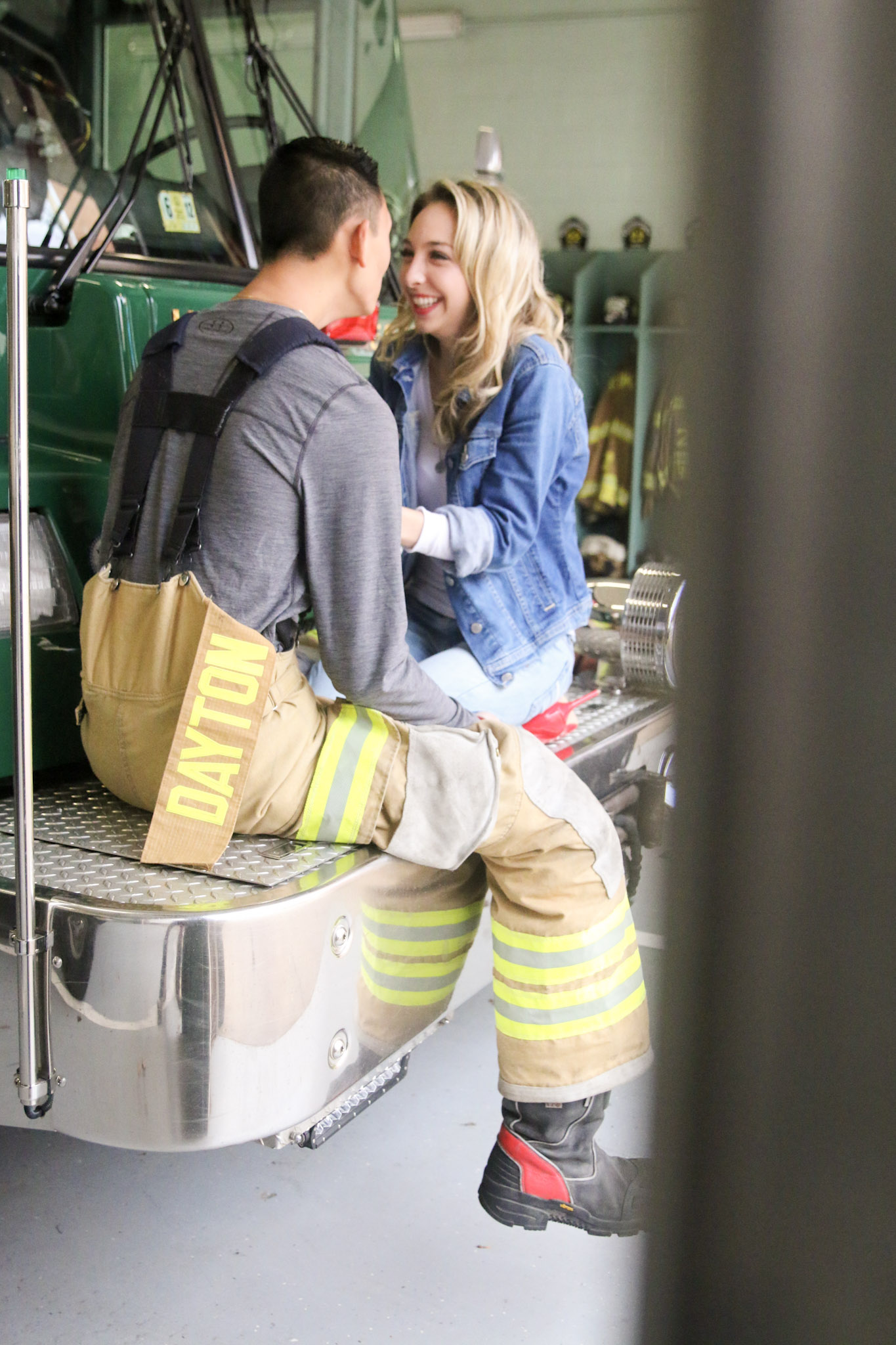 The young lady laughs as she kneels in front of her young boyfriend, who is seated in front of her.