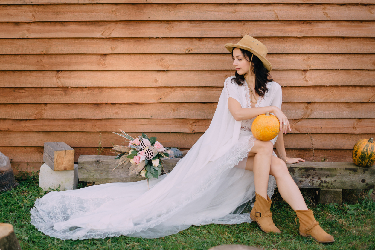 A lovely young bride with cowboy boots sits admiring her bouquet.