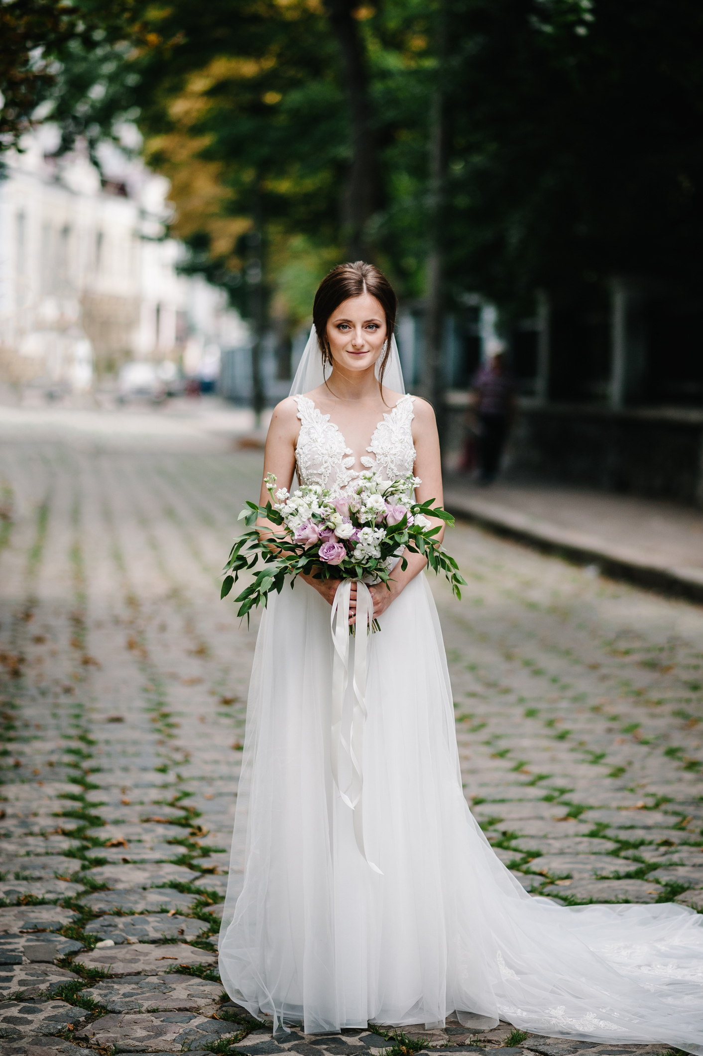 Young beautiful girl in elegant dress is standing and holding hand bouquet of pastel pink flowers and greens with ribbon at nature. The bride holds a wedding bouquet outdoors.