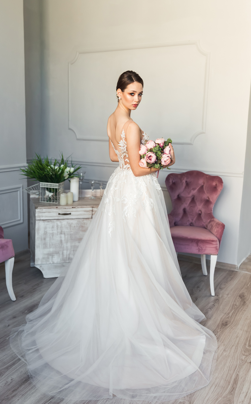 charming and youthful bride beaming with smile adorned with her beautiful white lace wedding dress holding her bridal bouquet.