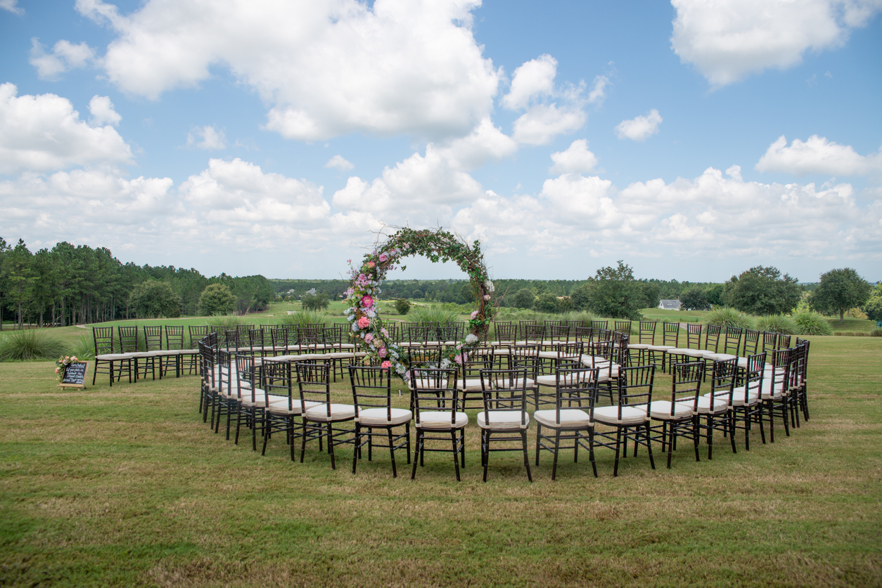 Unique round spiral chair pattern wedding ceremony setting at rolling hills countryside with brown chiavari chairs and white cushions