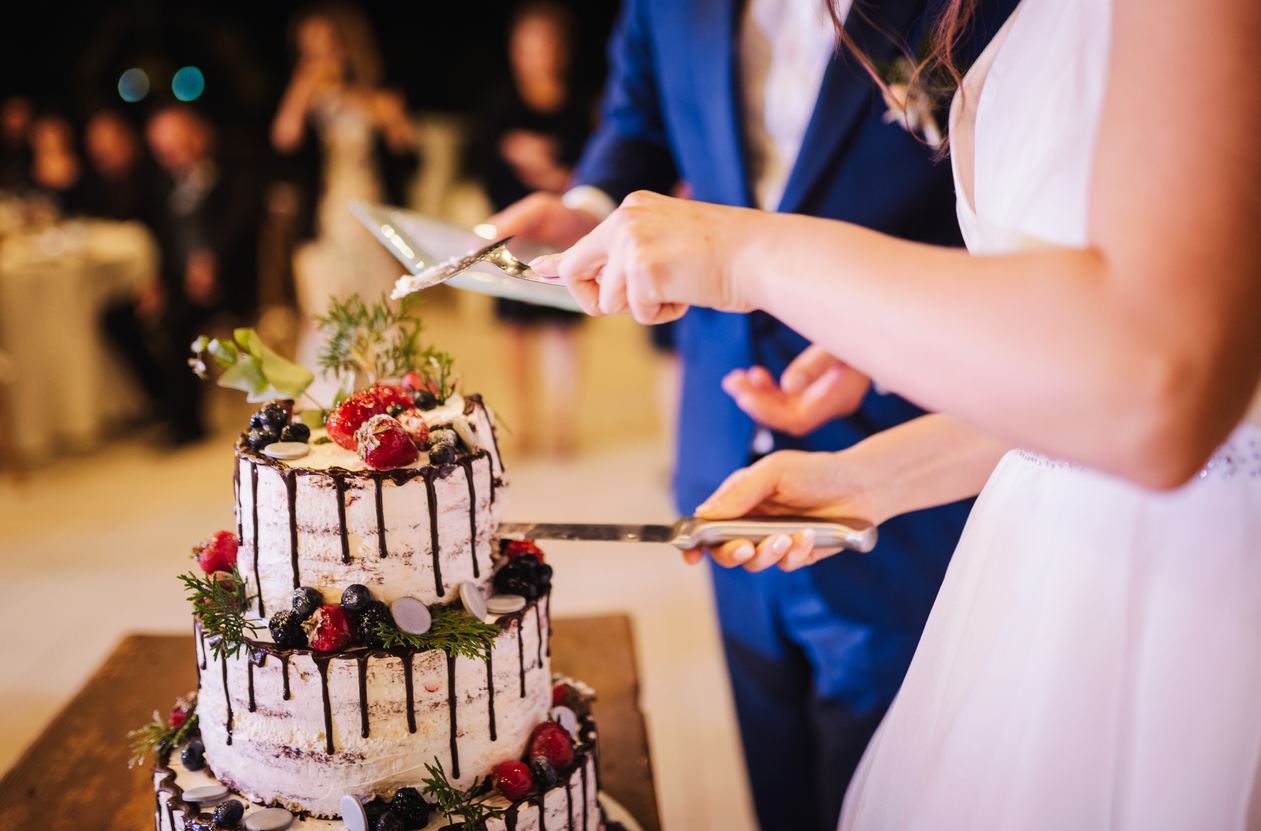 the groom and the bride cutting their light buttercream wedding cake with berries.