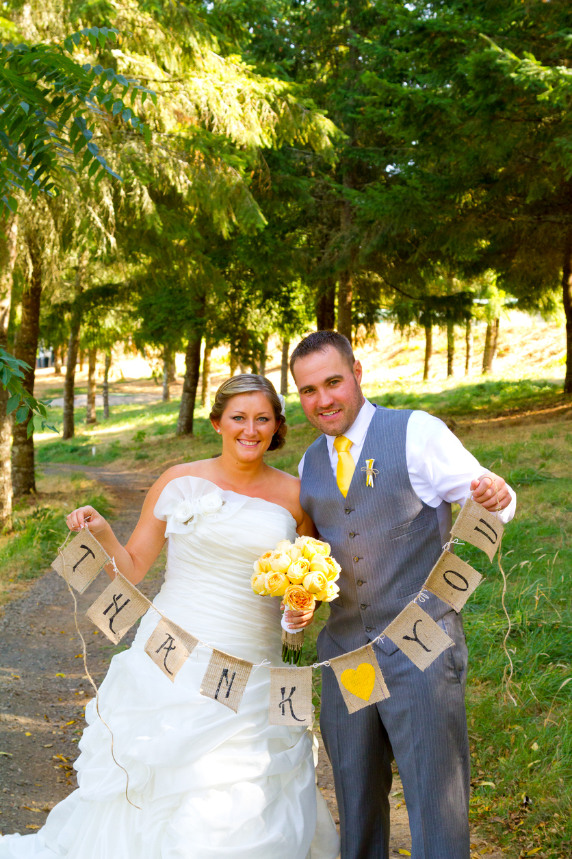 A bride and groom hoist a burlap banner that says "thank you" so they may use it for thank you cards later.