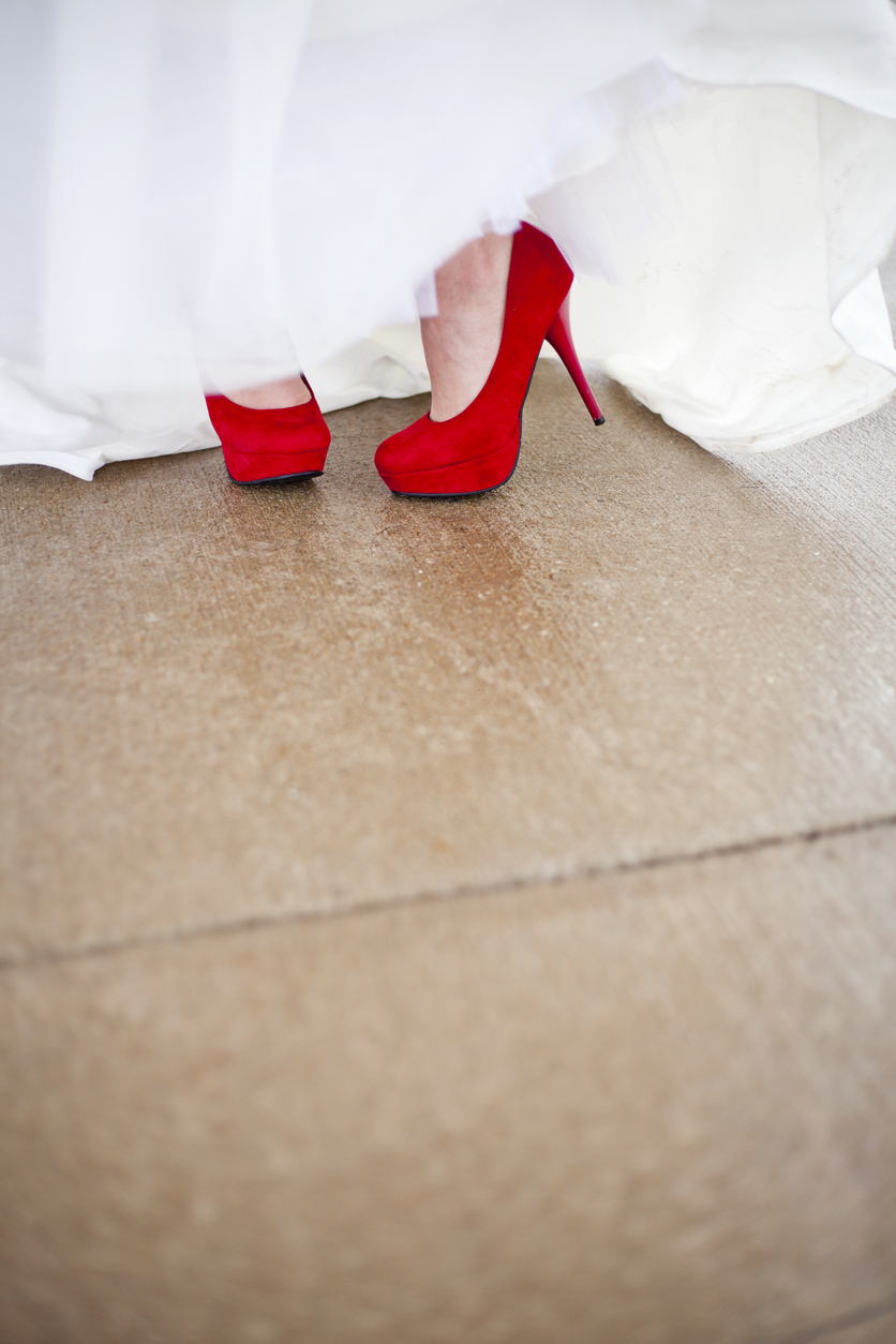 A woman in a white wedding dress is wearing red buckskin leather high heels.