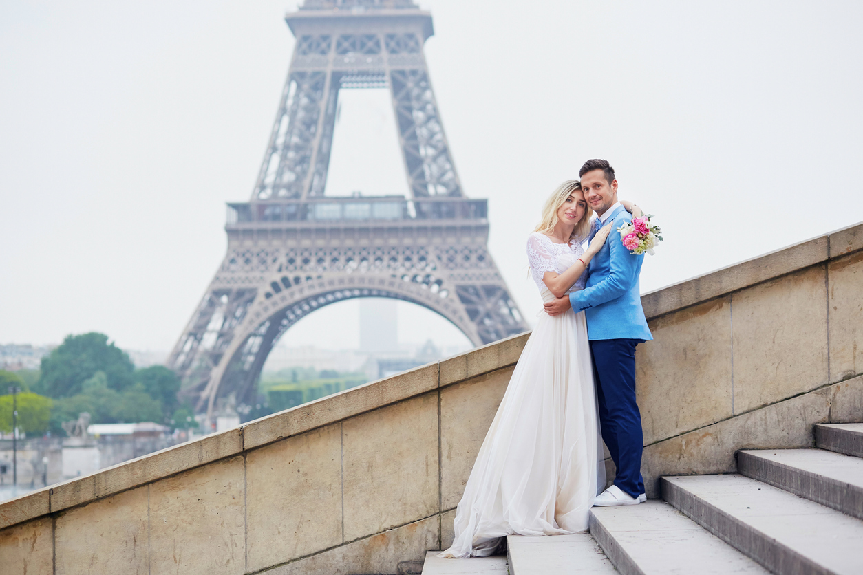 a newlywed couple dressed in elegant wedding attire stands close to the iconic Eiffel Tower, which looms majestically in the background. They are in the heart of the city of love, Paris, France.