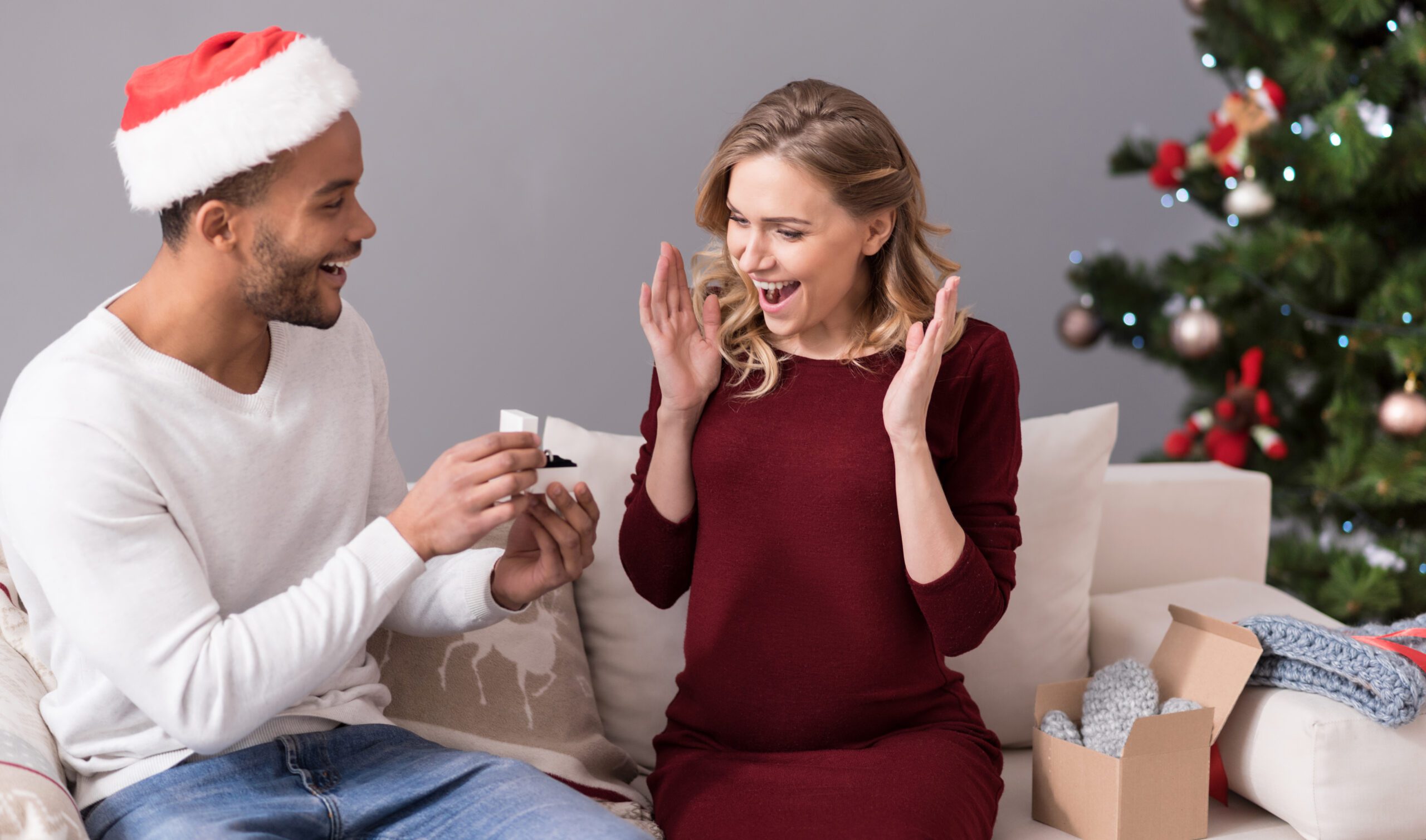 Expensive gift. Good looking cheerful young man holding a small box and showing the ring to his girlfriend while giving her a present