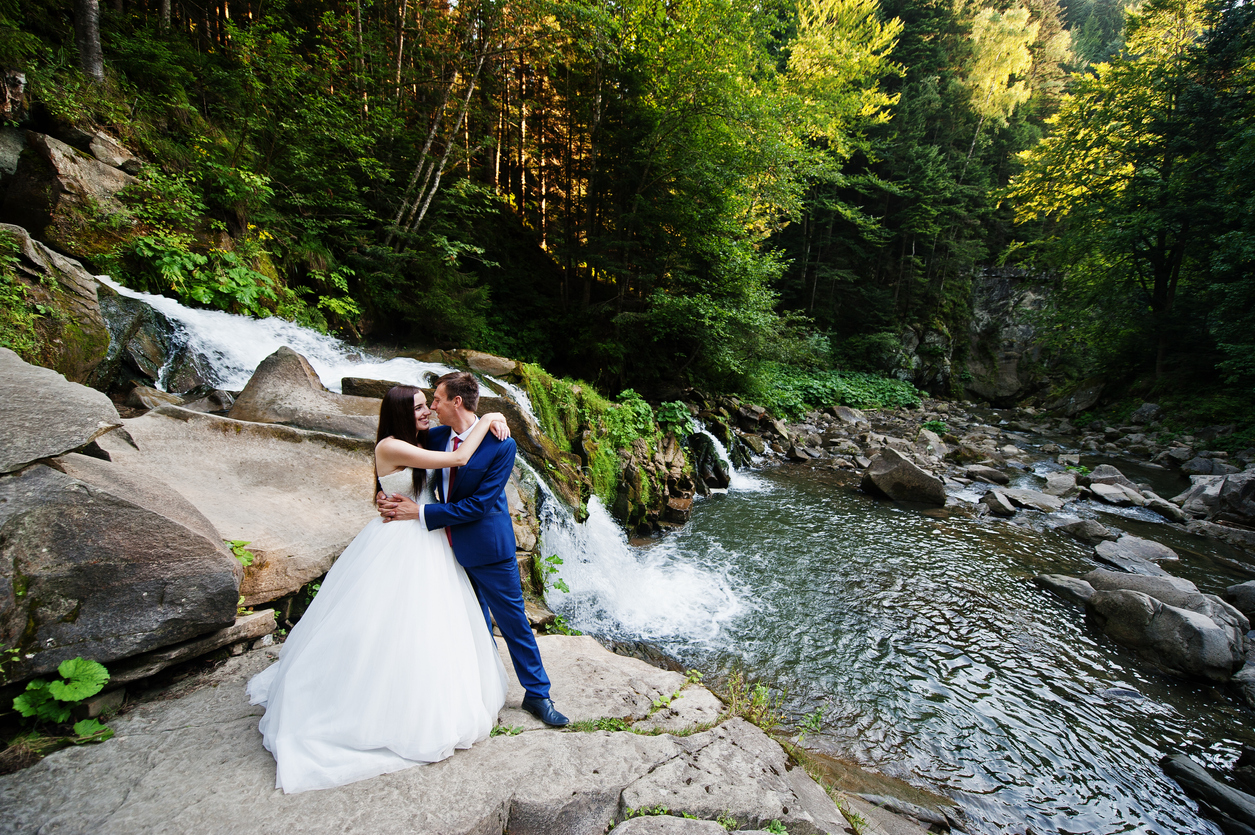 Beautiful wedding pair against a waterfall at sunset in the Carpathian Mountains.