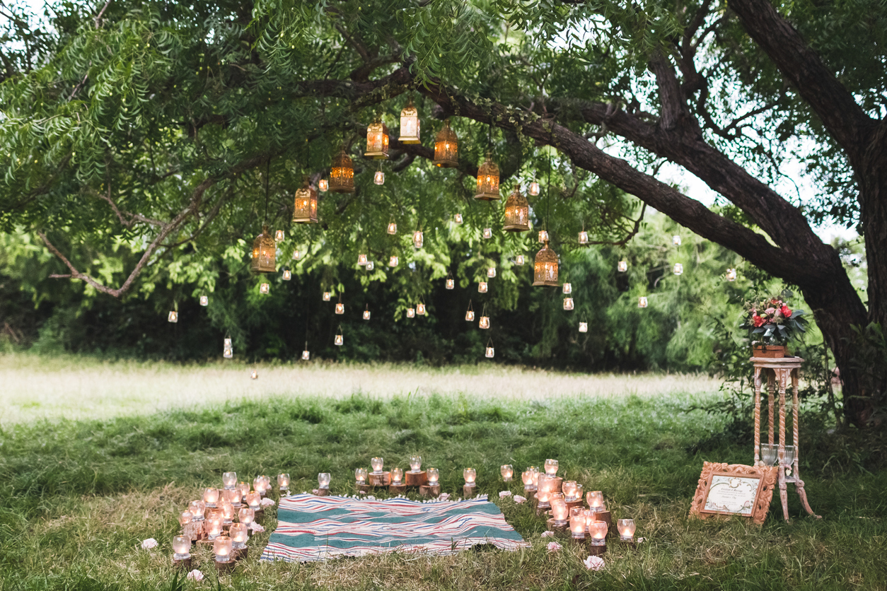 Evening wedding ceremony with a rug and lot of vintage lamps and candles on big tree. Rustic style