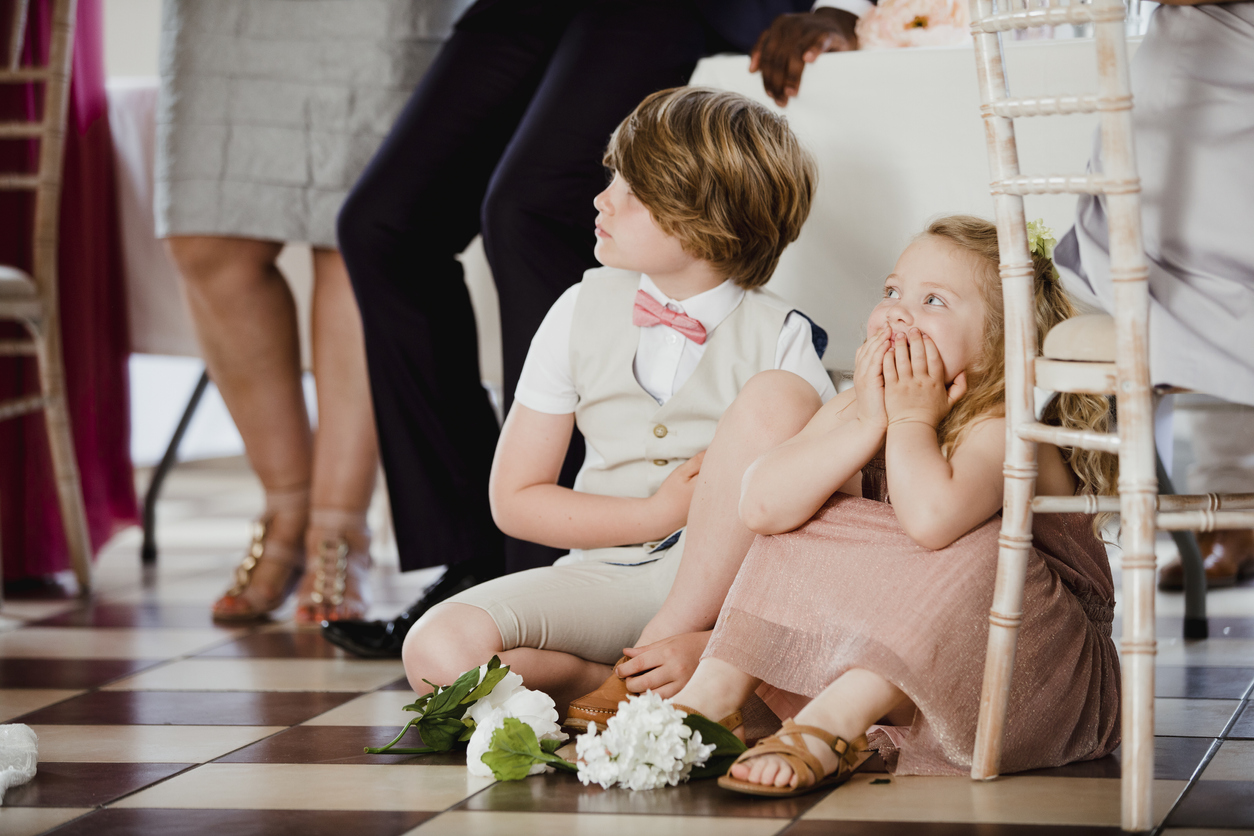 Children are sitting on the dancefloor by a table at a wedding. 