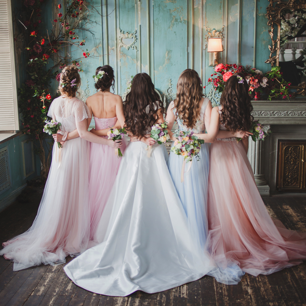 Bride and bridesmaids. Beautiful young women in dresses and with bouquets of fresh flowers. Back view