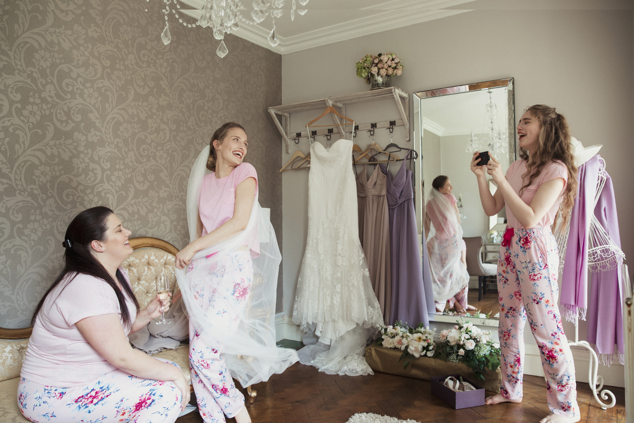 On the morning of her wedding, the young lady photographed a woman who was wearing a veil in a humorous manner. She's standing with a bridesmaid, and they're all giggling in matching pajamas.