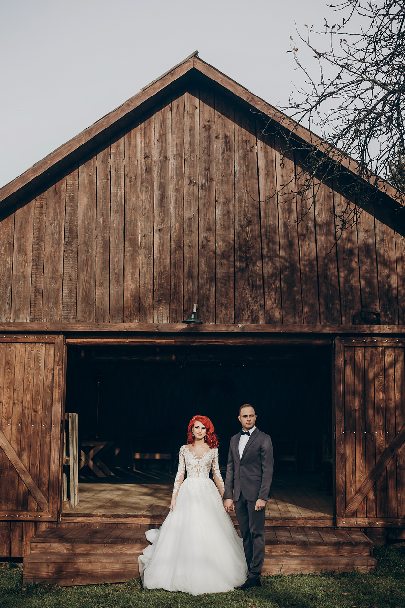 A beautiful bride and groom pose and stand in front of a wooden barn. 