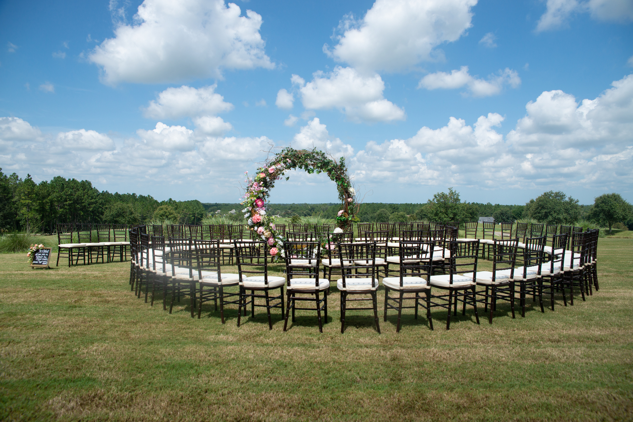 Unique round spiral chair pattern wedding ceremony setting at rolling hills countryside with brown chiavari chairs and white cushions