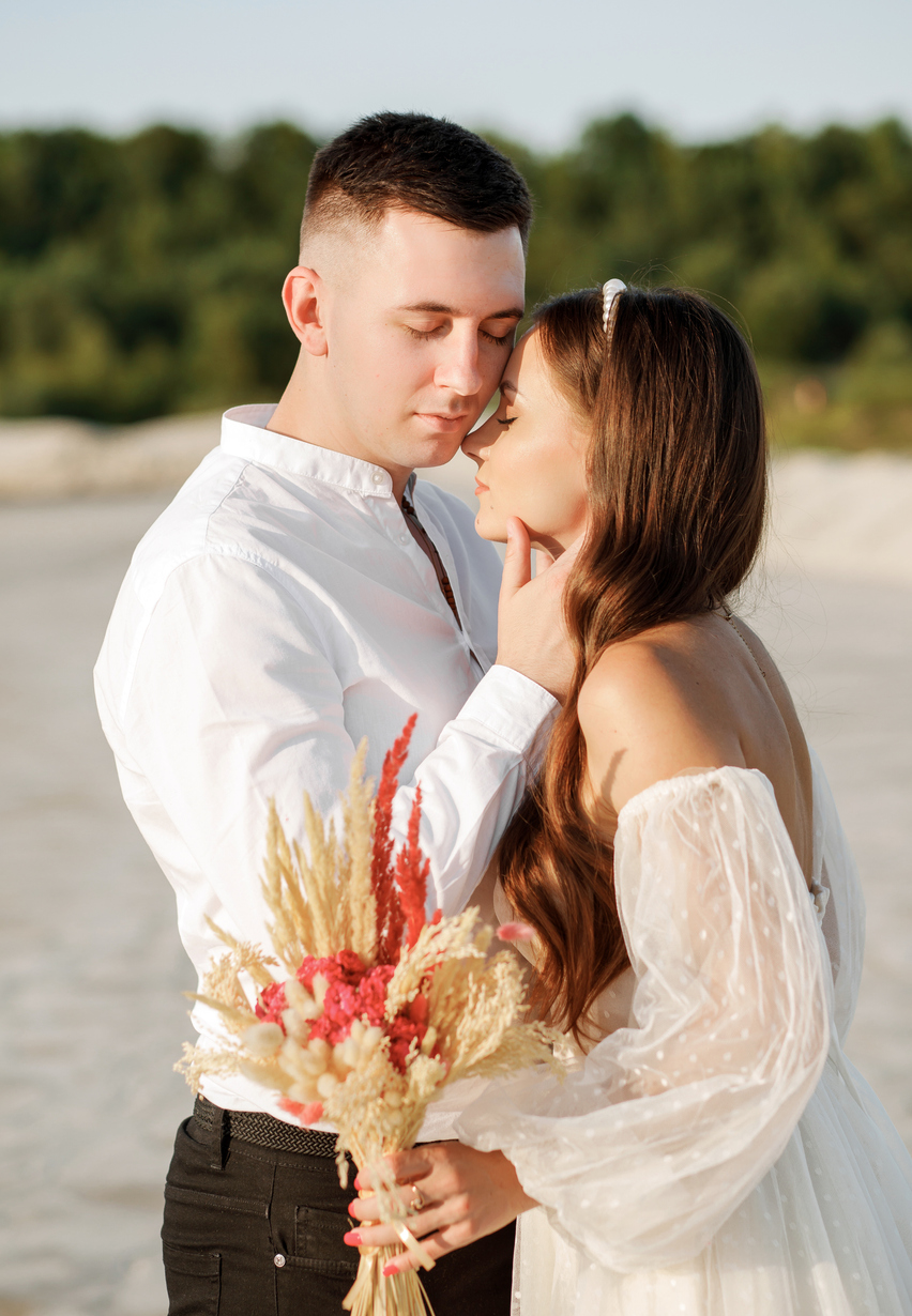 Unusual wedding in the desert. A girl in a white dress ivory shade. A loving couple is embracing tenderly against the background of white sand and green forest