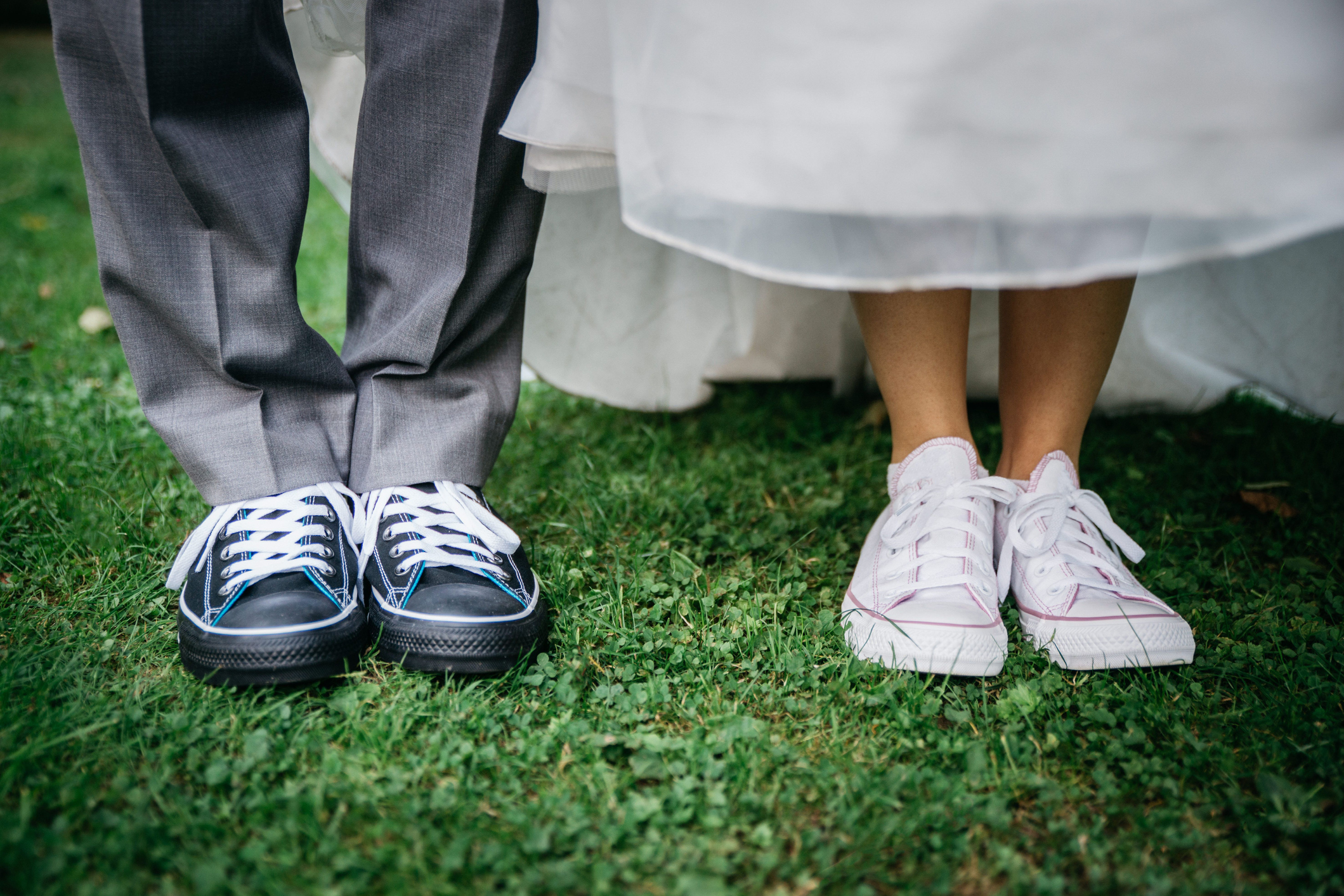 Legs of groom and bride wearing sneakers and standing on the green grass in the park