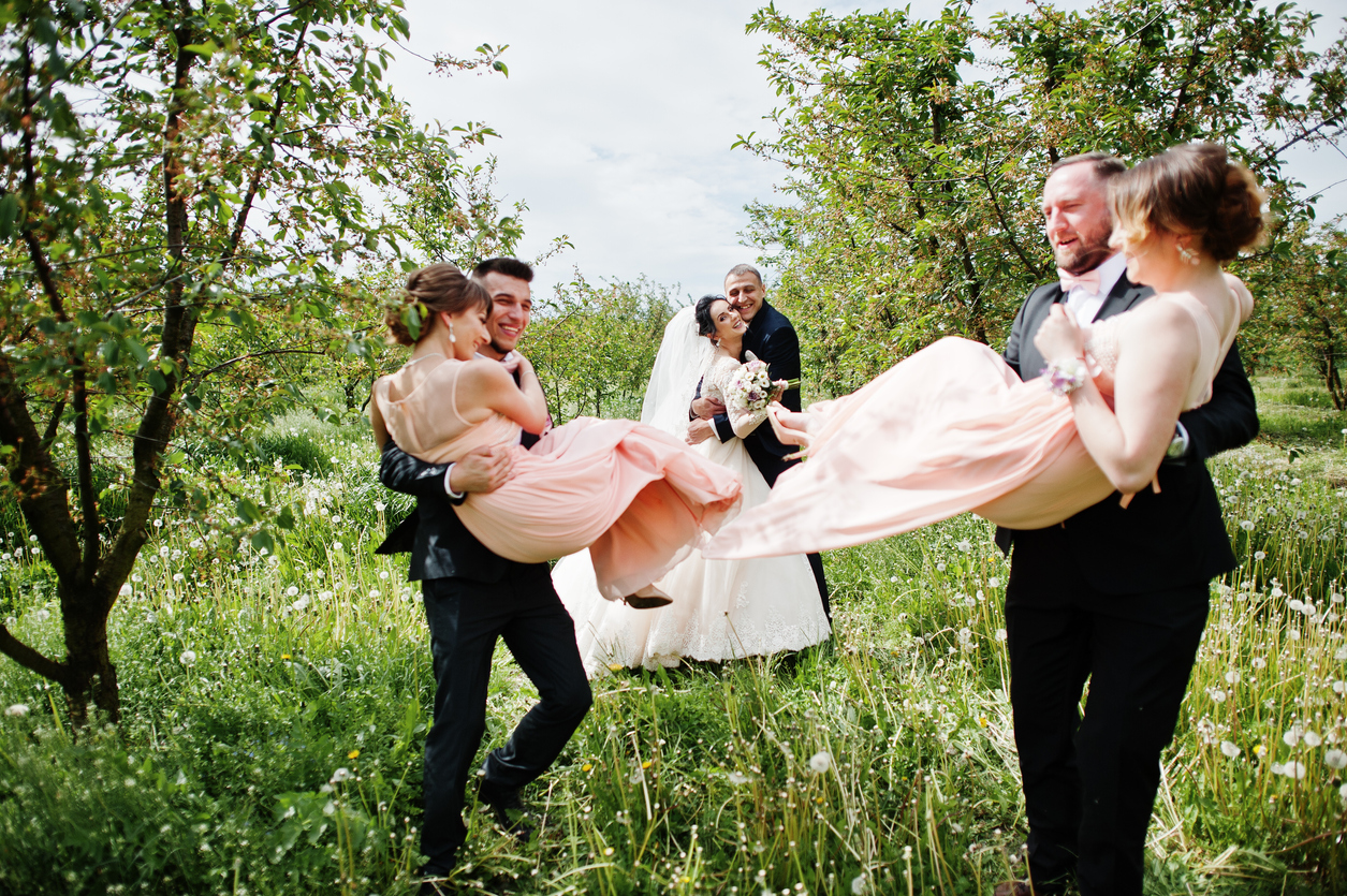 Wedding couple standing and looking at groomsmen spinning bridesmaids in their hands.