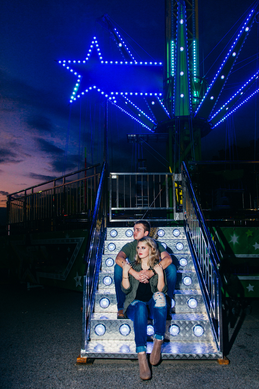 a young Caucasian couple sit on the illuminated stairs of a thrill ride.