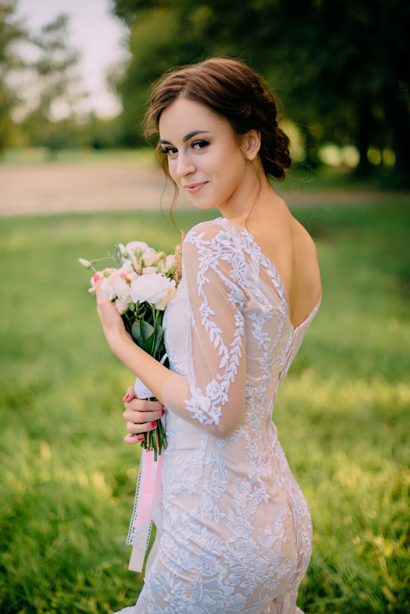 bride stands in summer garden with bouquet in her hands