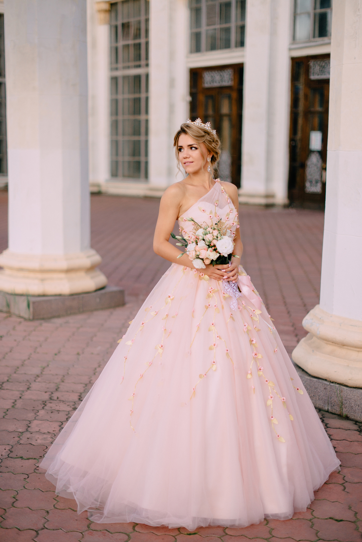 bride with bouquet in her hands stands on background of architecture