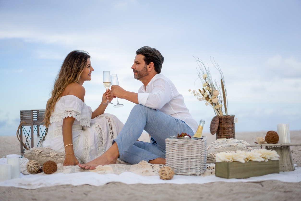 loving couple on a romantic date at the beach making a toast with glasses of champagne and looking very happy.