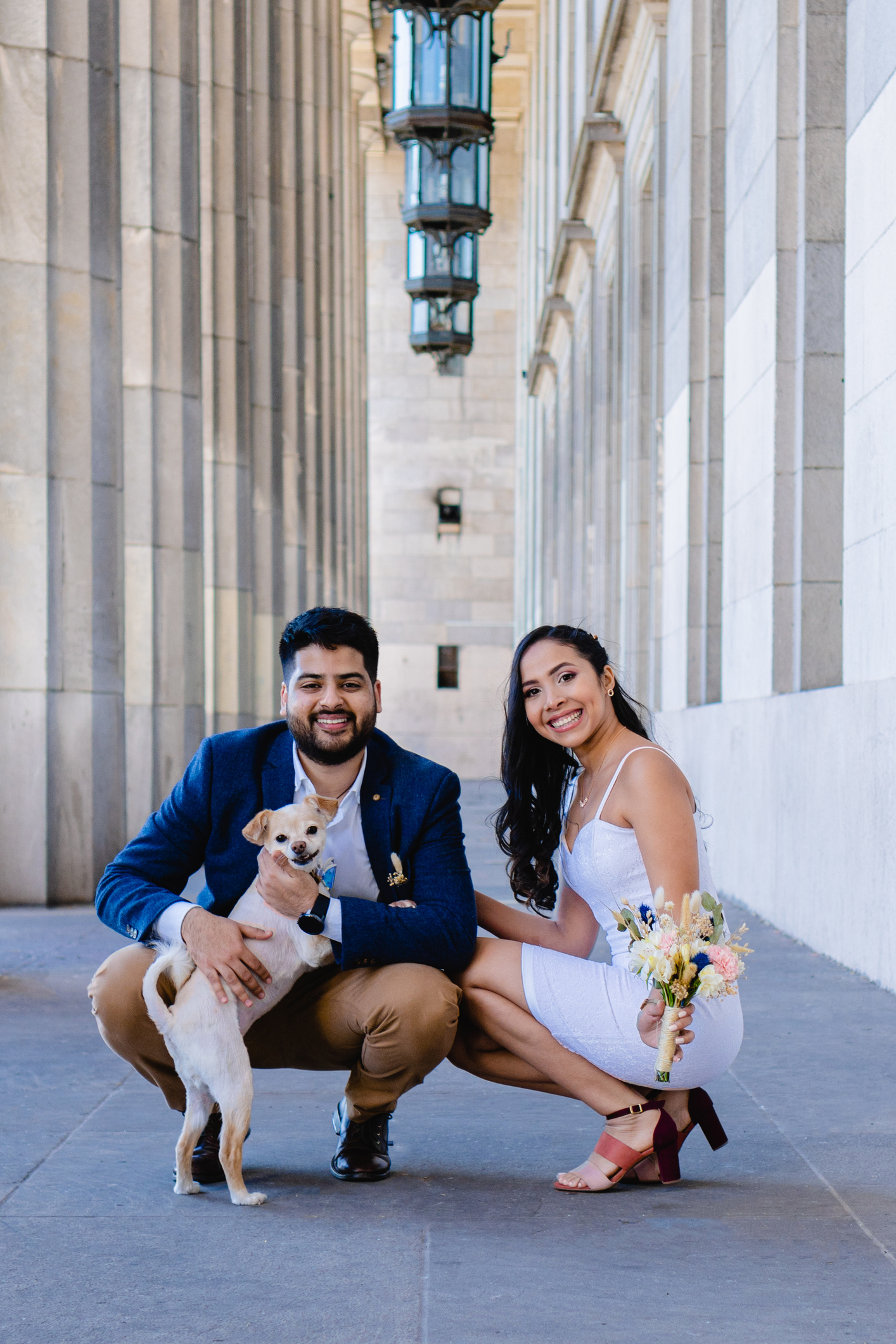 latin and modern bride and groom smiling with a pet, dog. looking at camera, vertical and artistic picture