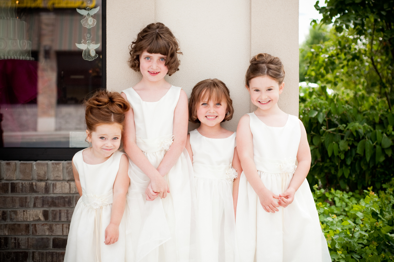 Color photo of four happy little flower girls standing together while wearing formal dresses.
