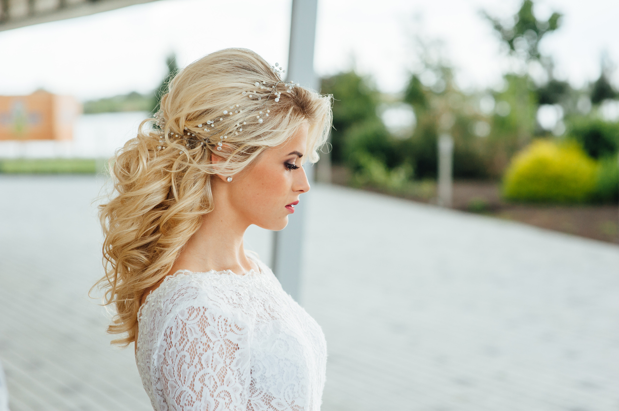 gorgeous young bride in a fancy wedding gown with red lips makeup and a beautiful wavy half-up hairstyle.