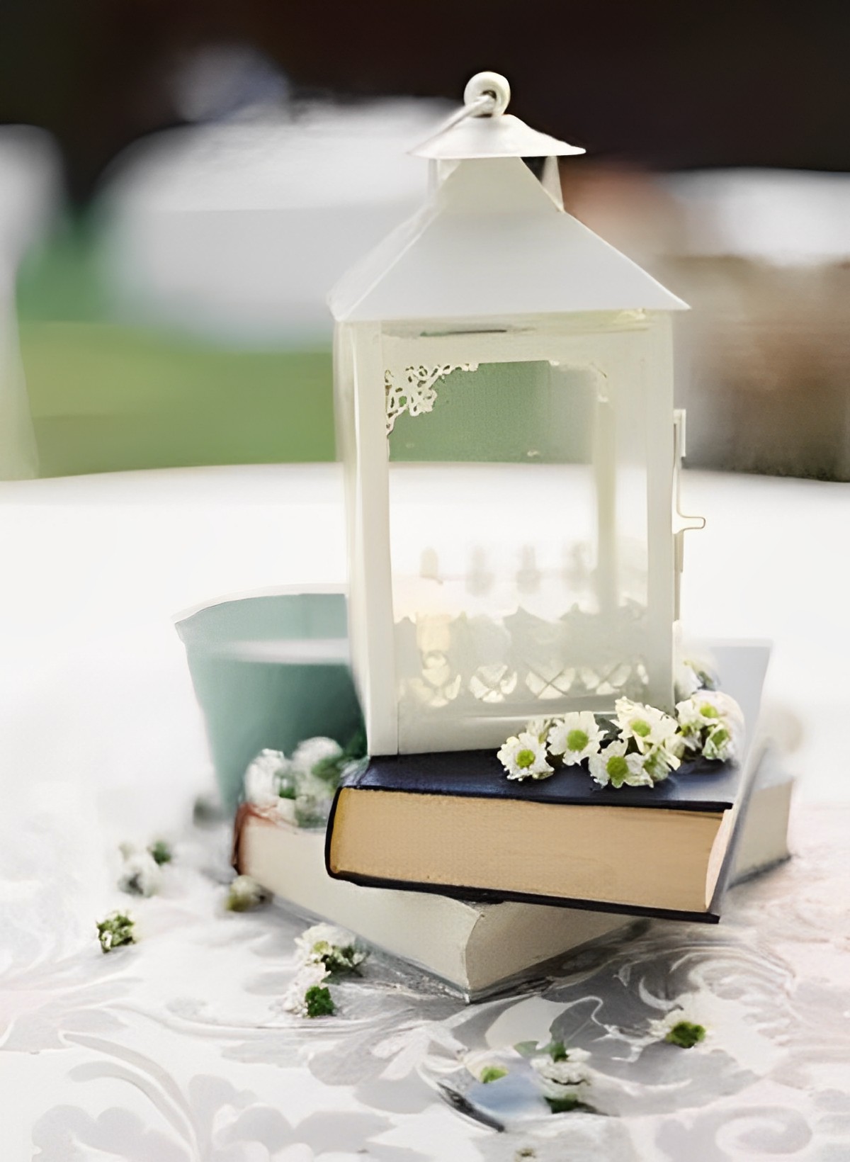 This lantern has a timeless and flexible design on top of a book with little white flowers surrounding it.