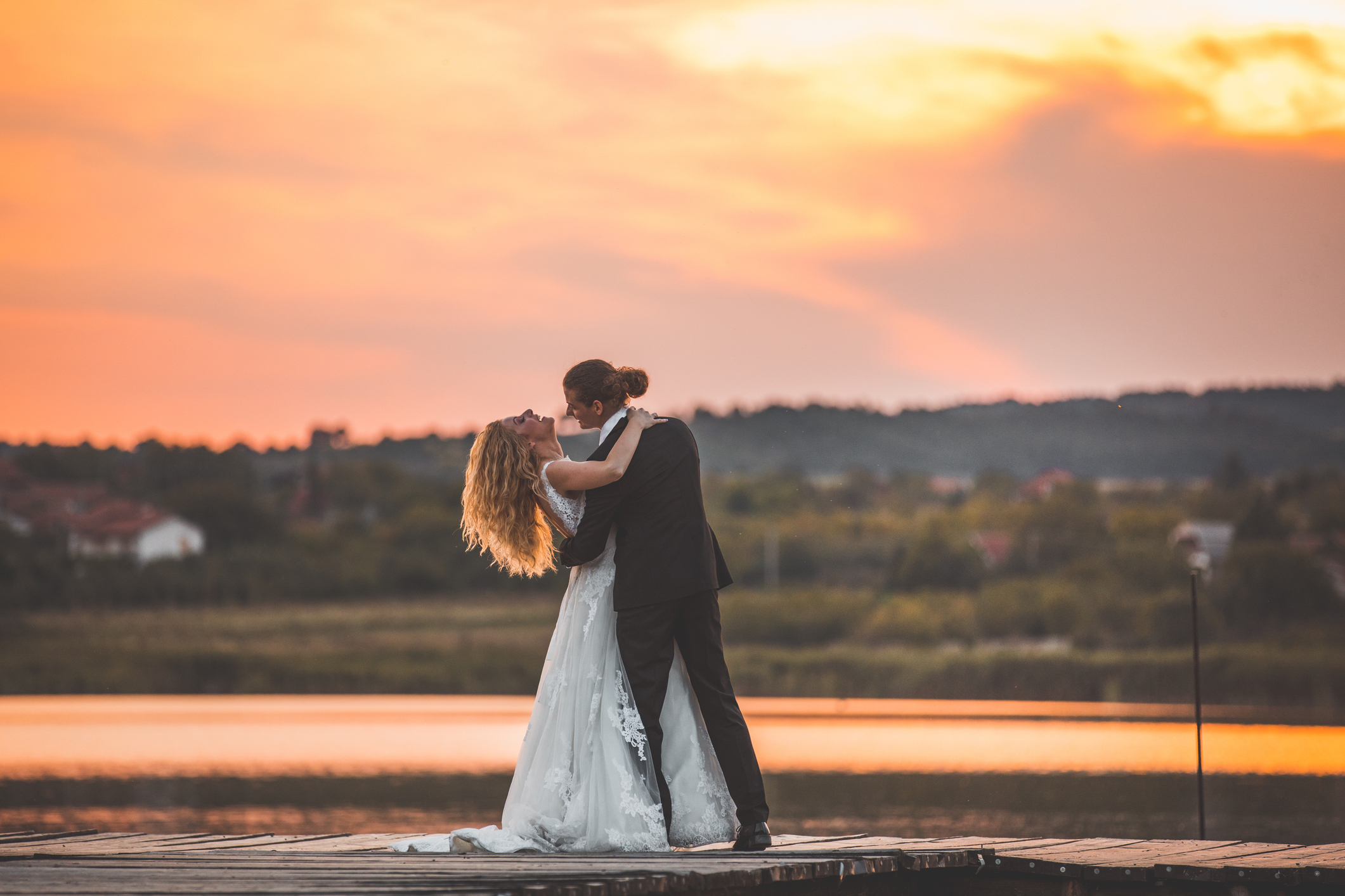 Happy newlywed couple dancing on like pier at sunset