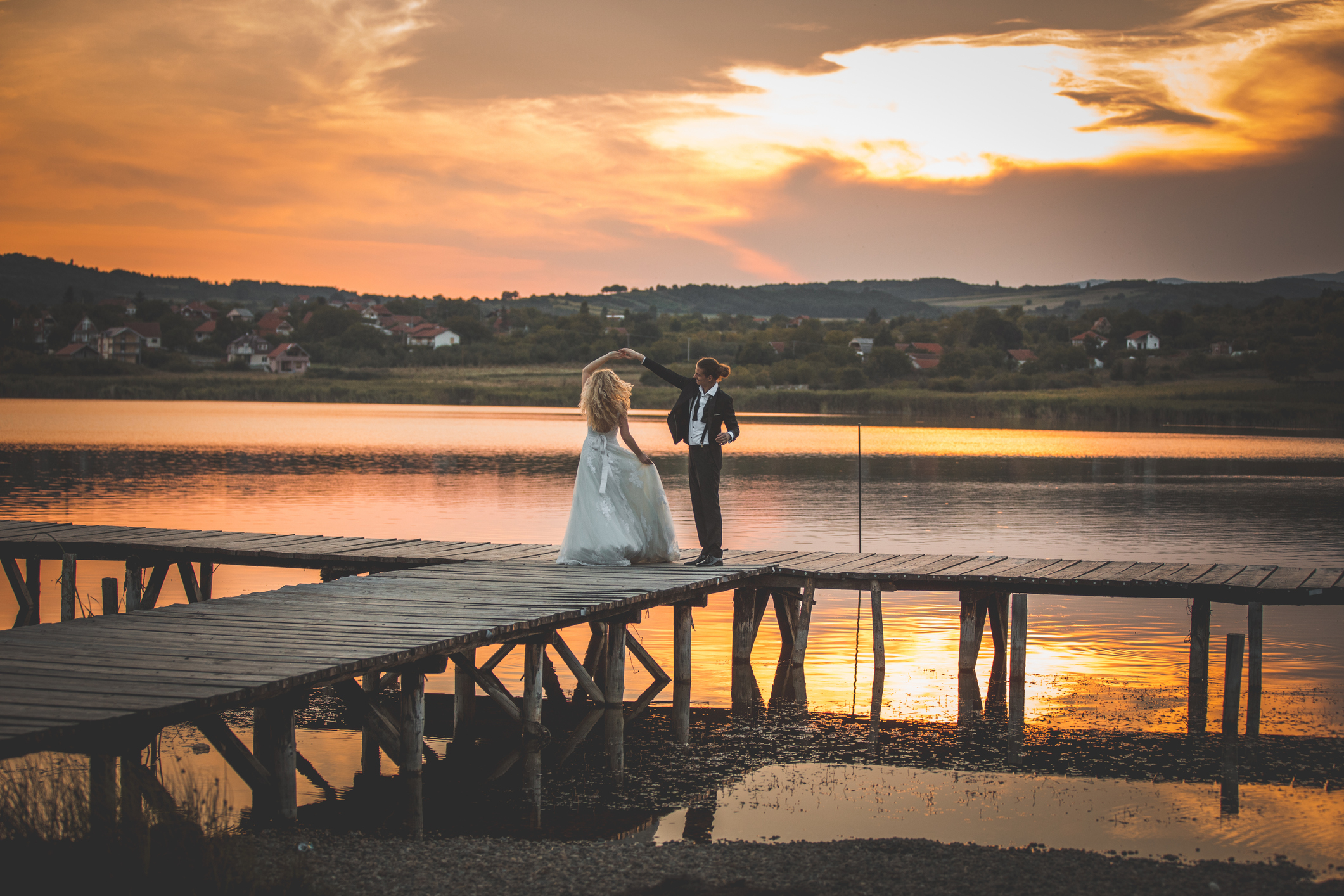 Happy newlywed couple dancing on like pier at sunset