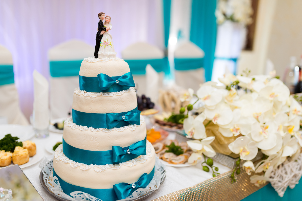 gorgeous white wedding cake with light blue ribbon and a crystal in the centre of the ribbon, as well as a simple design on the cake,