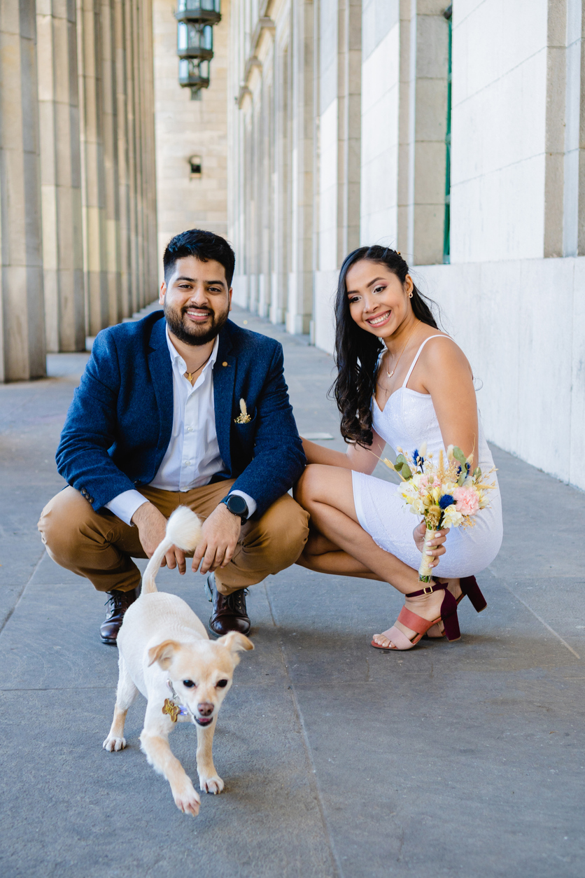 latin and modern bride and groom smiling with a pet, dog running to camera, vertical and artistic photo