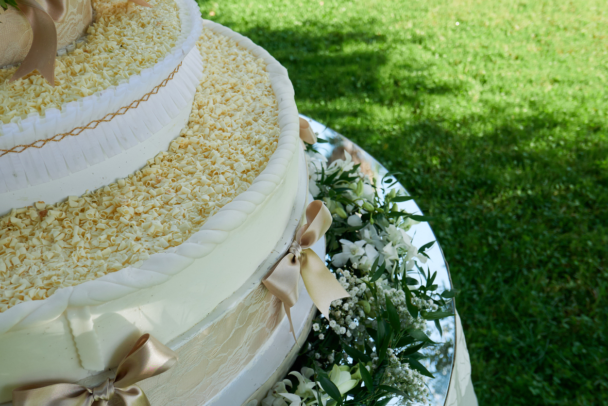 A close-up of a wedding cake with a gold ribbon design and shredded cheese toppings.