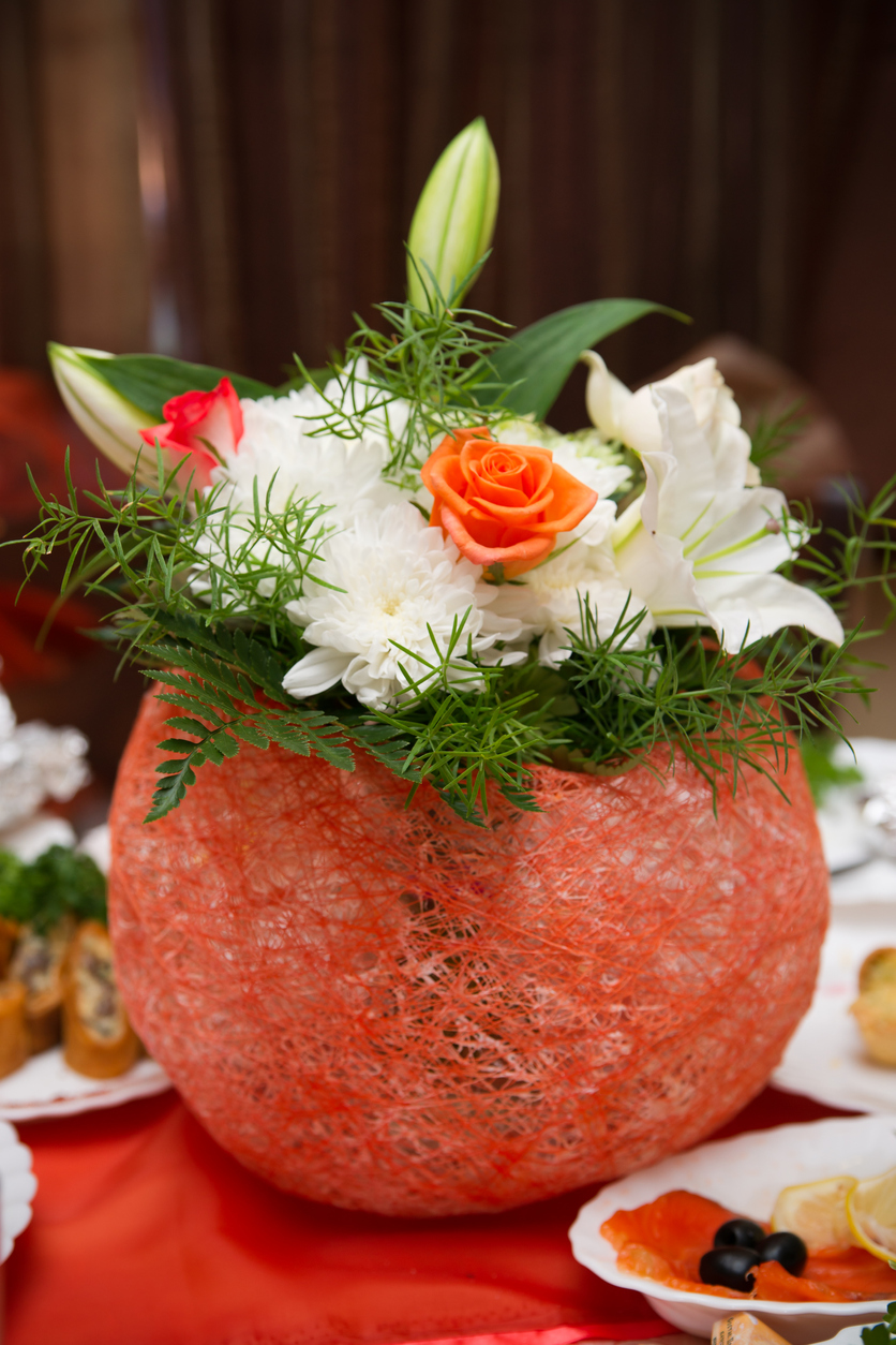 a spherical red lantern with fresh flowers and some green leaves as centerpiece