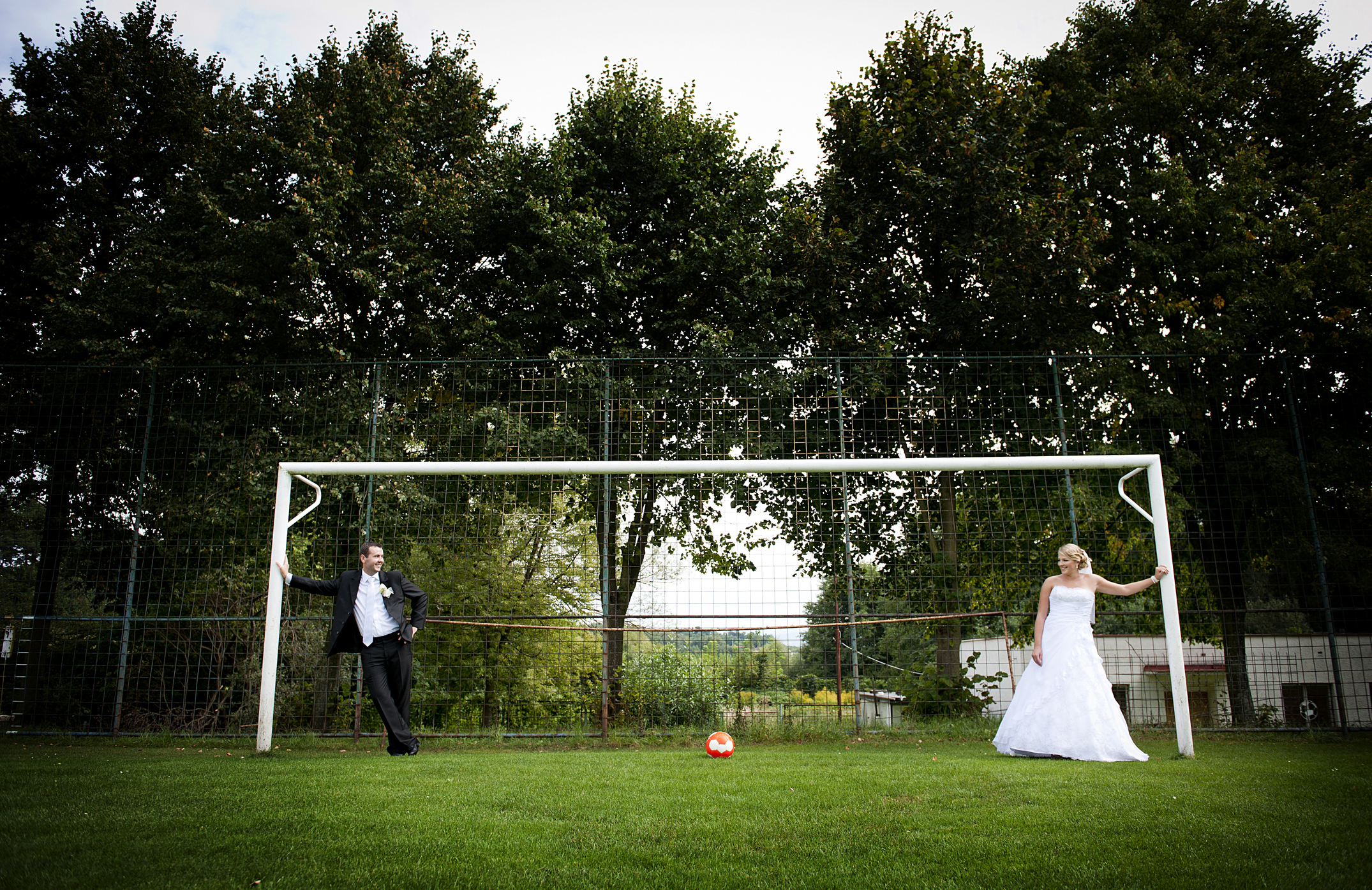 bride and groom are playing at the football pitch