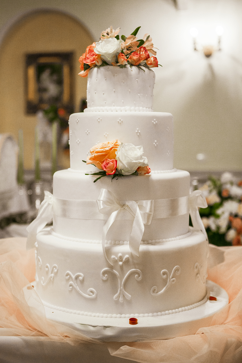 Elegantly constructed four-tiered wedding cake with ribbon and floral embellishments.