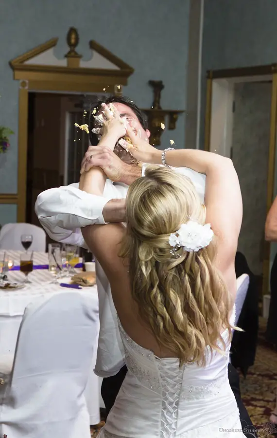 the bride smashing a piece of cake into her husband's face during their wedding ceremony.