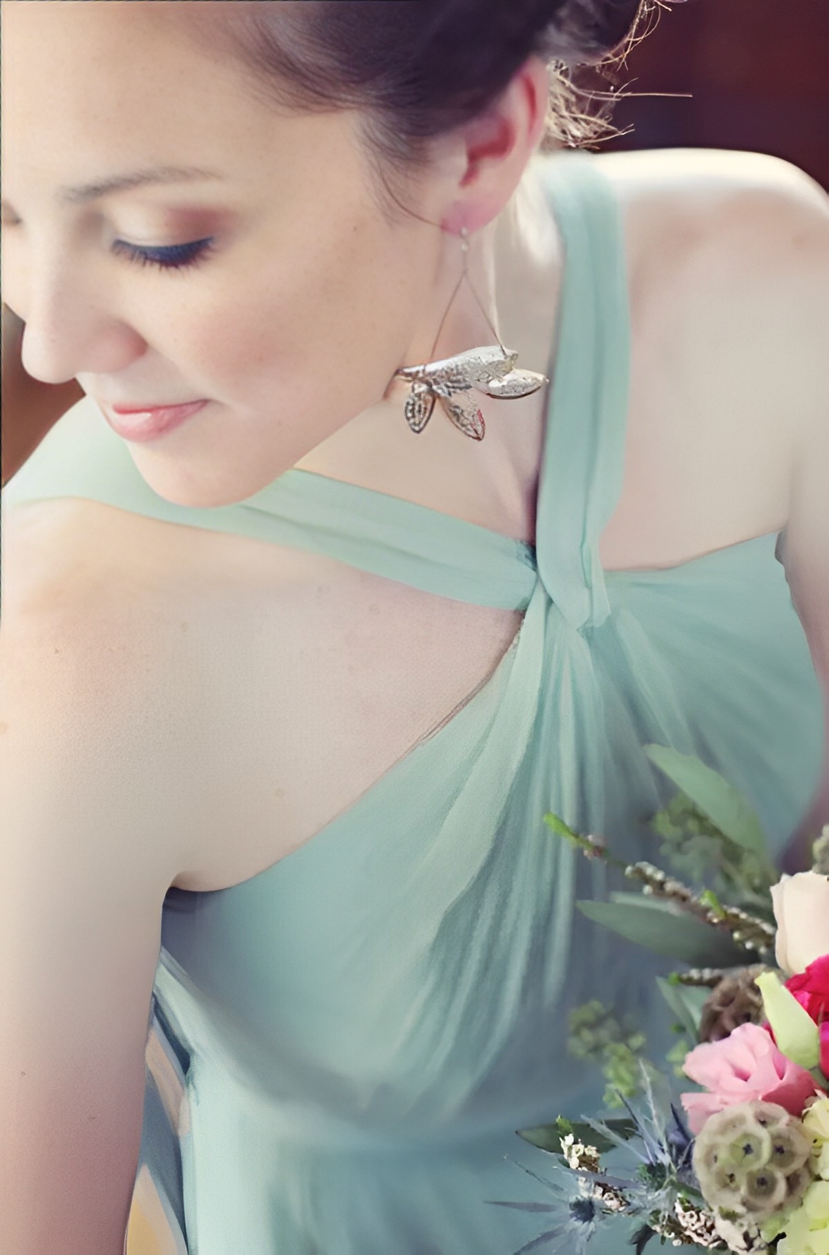 A gorgeous bridesmaid in a silky sage green gown, holding her bouquet and wearing a crystal earring. 