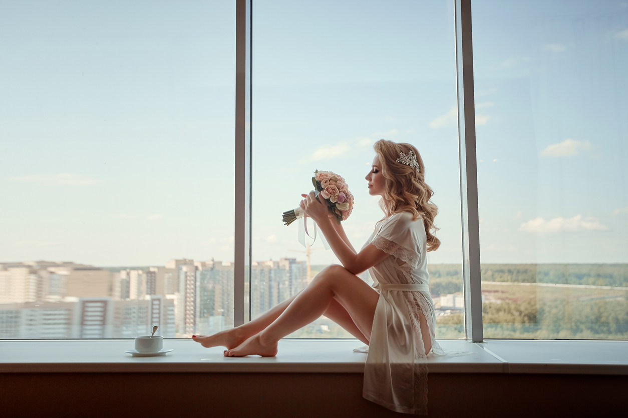 Picture of a lovely young bride. With a bouquet, she sits by the window.