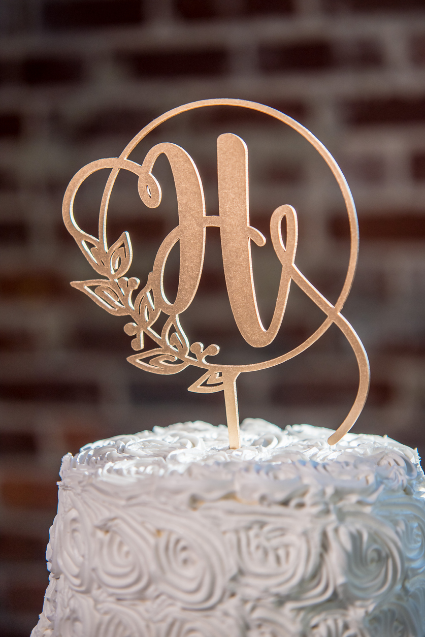 A vertical closeup shot of a H-shaped topping on a beautiful white wedding cake