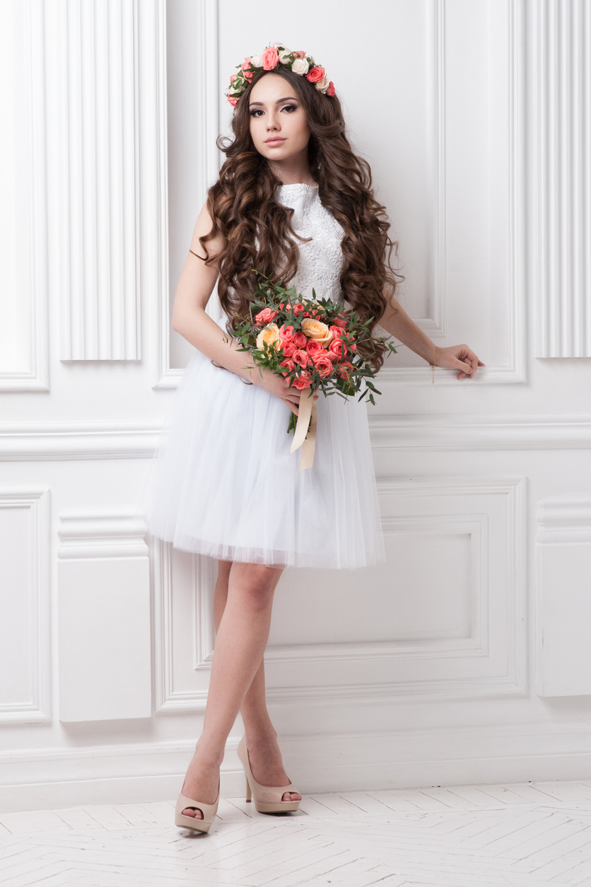 a youthful and attractive bride is grasping her wedding bouquet, which complements her floral headpiece.