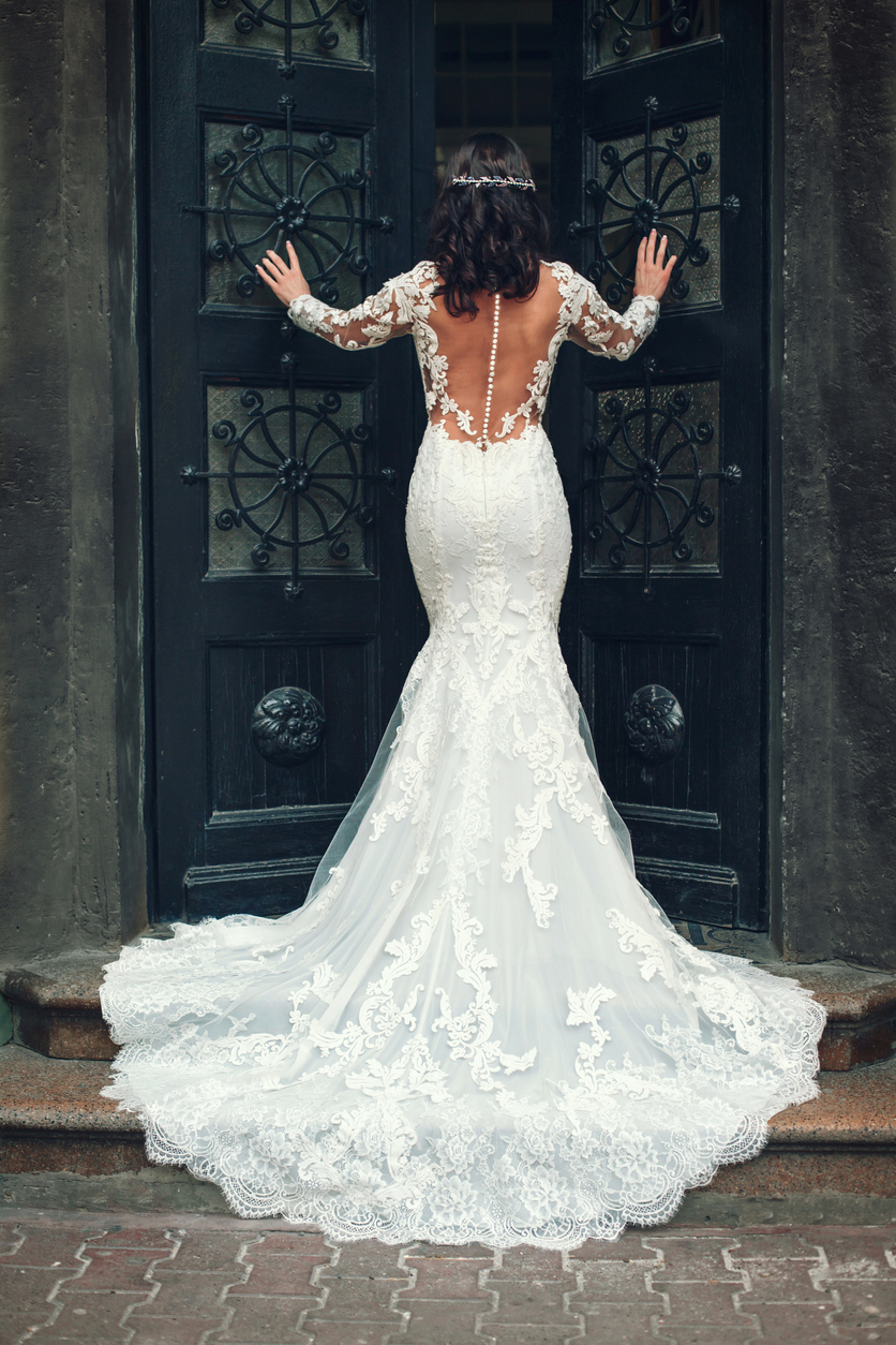 the bride in a sensual and gorgeous bridal gown with a headpiece facing the door.