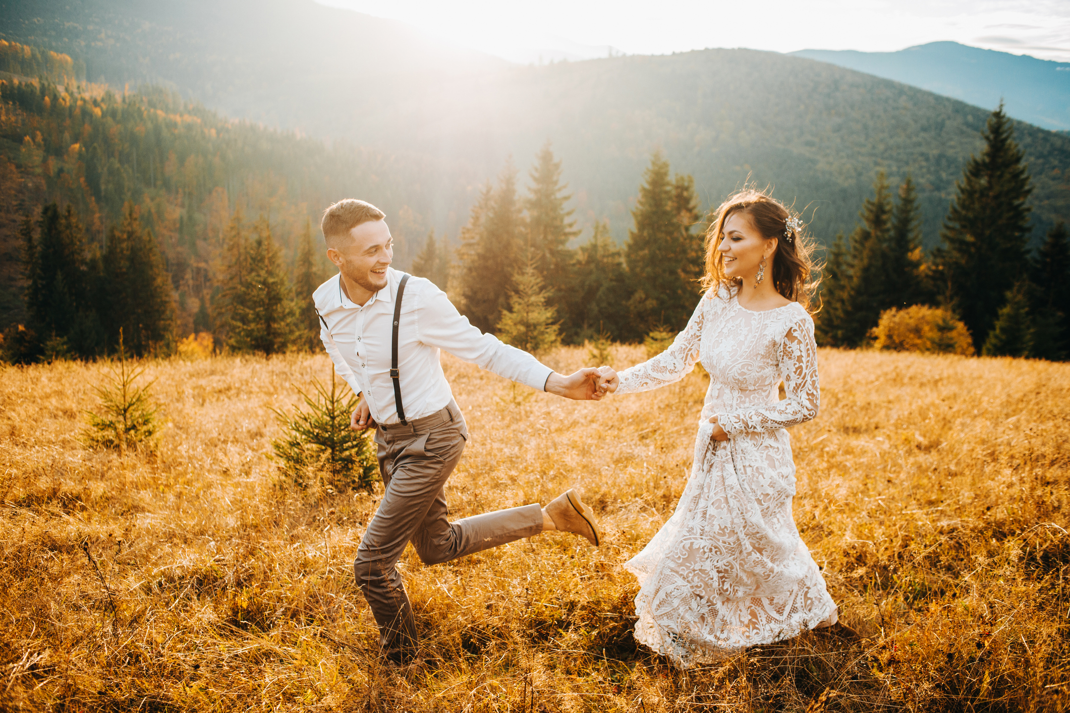 Sunset illuminates mountain hill where wedding couple walks. Fall wedding shoot.