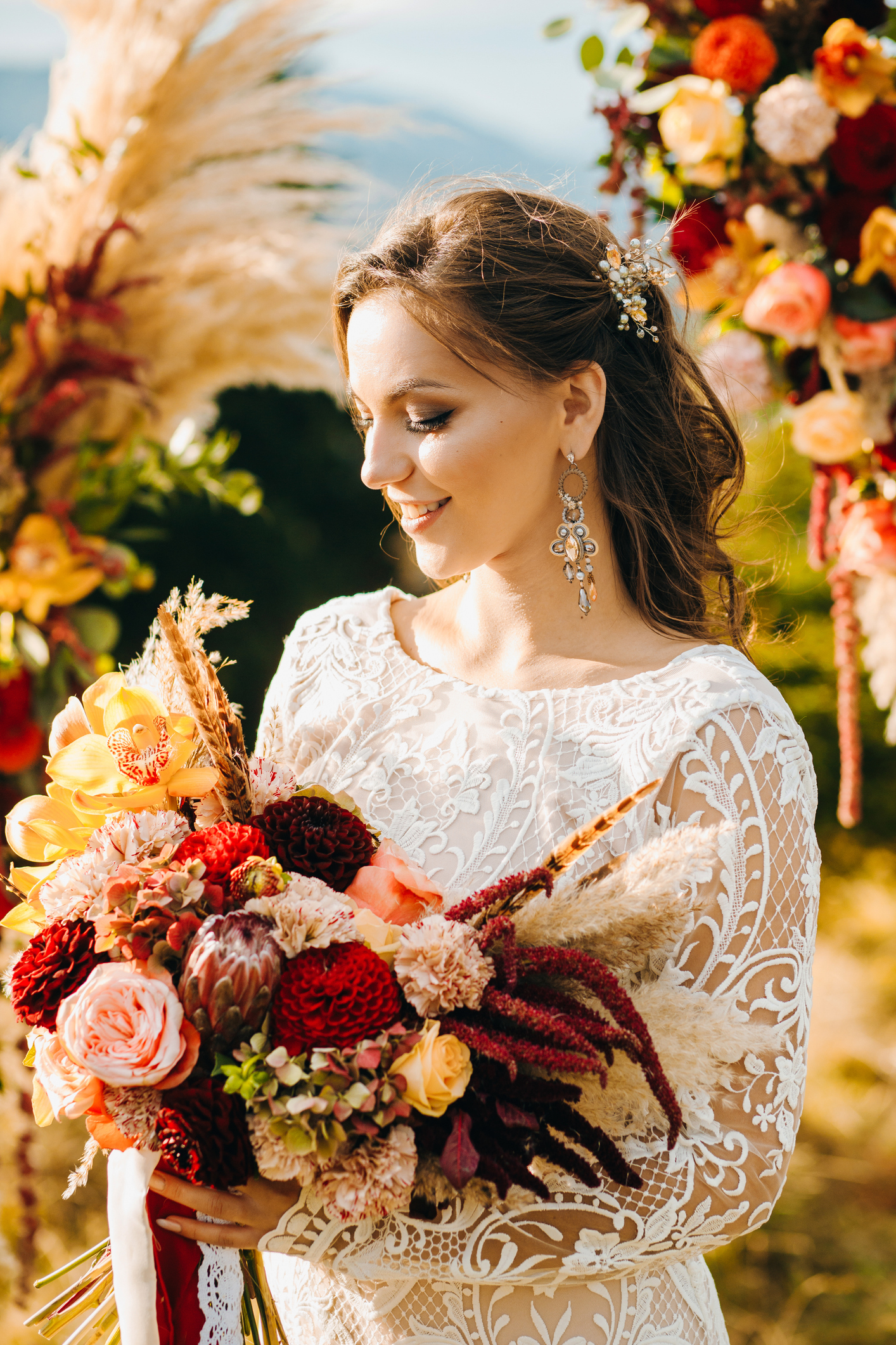 Happy bride in white stylish dress, with a wedding bouquet, beautiful mountains landscape in the background. Natural makeup, hairstyle. Fall wedding session.