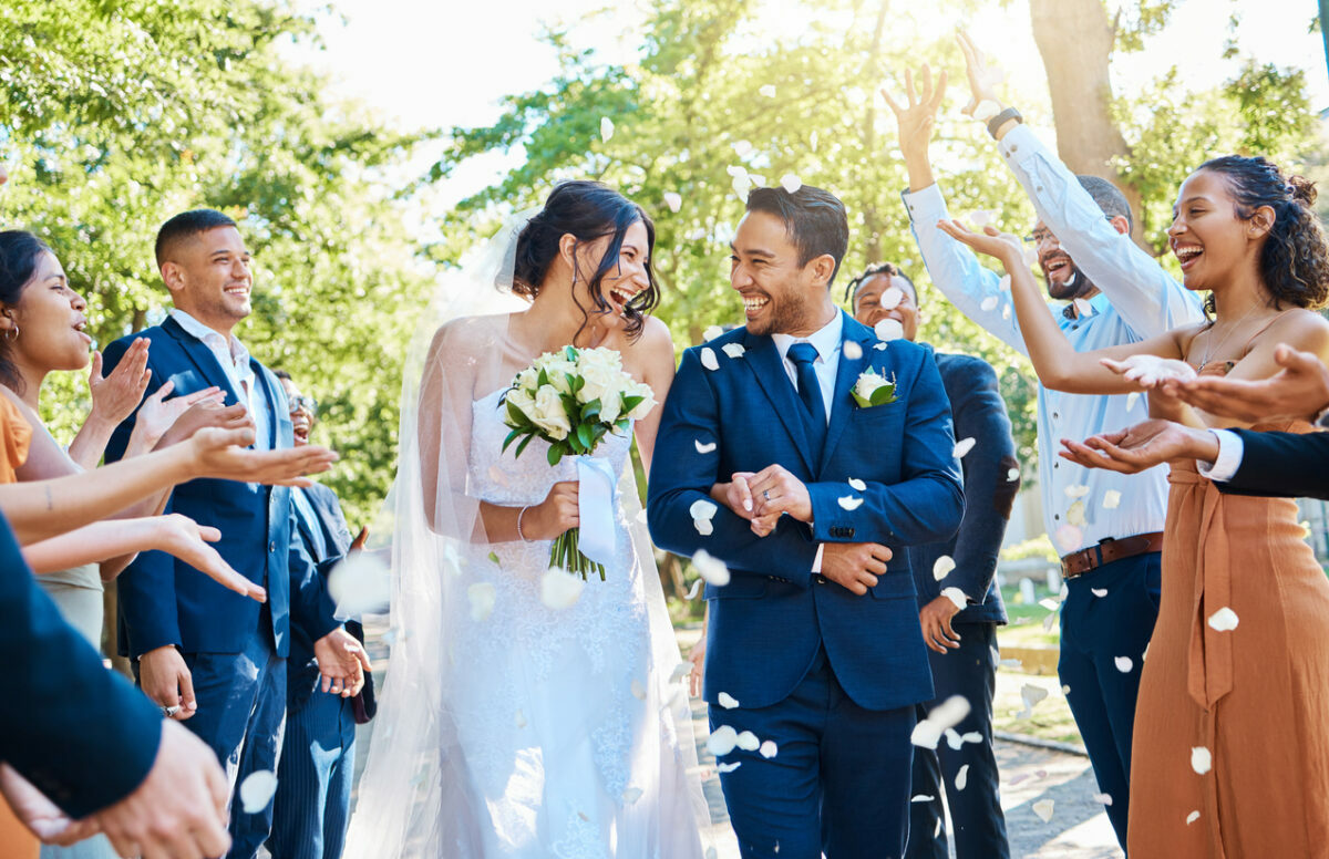 A lovely wedding departure by the newlywed couple, who are grinning with joy as their guests toss white rose petals in their path.