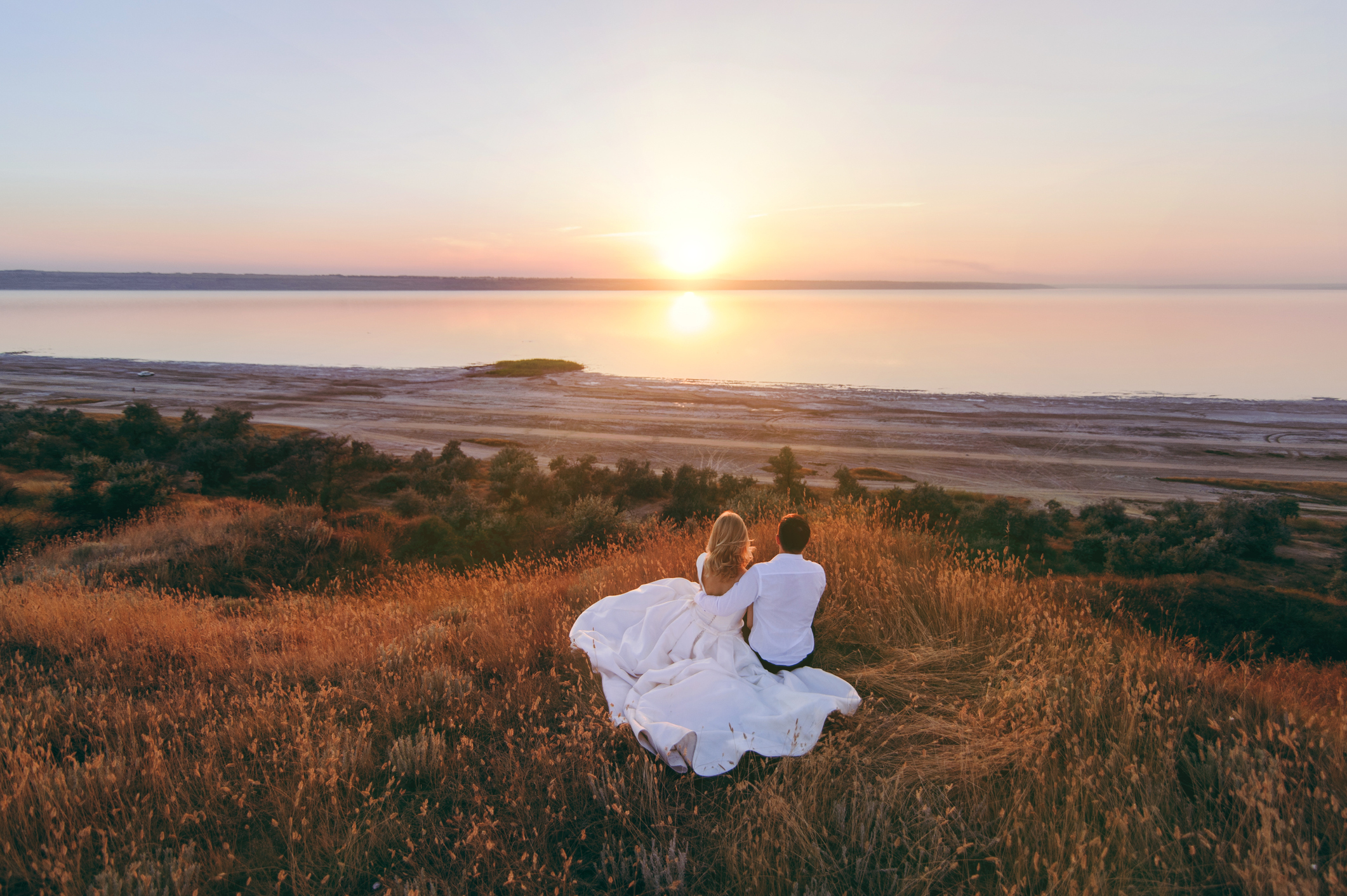 The bride and groom are walking together at sunset near the sea