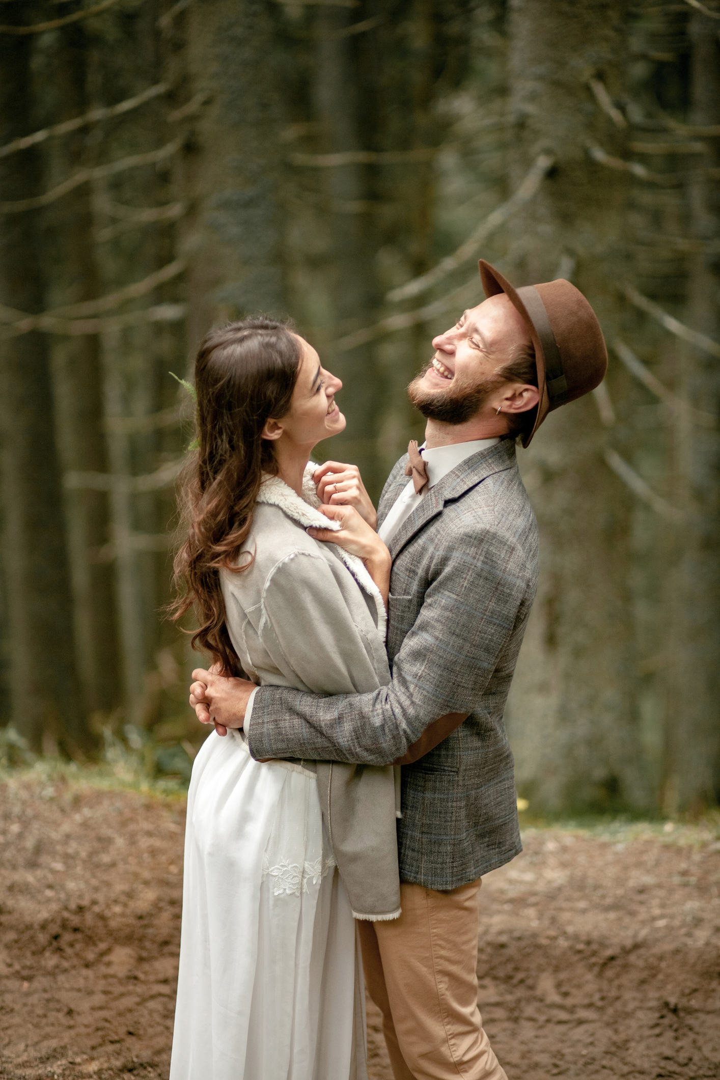 Bride and groom stand on forest road, embrace and laught gaily in Carpathian mountains.